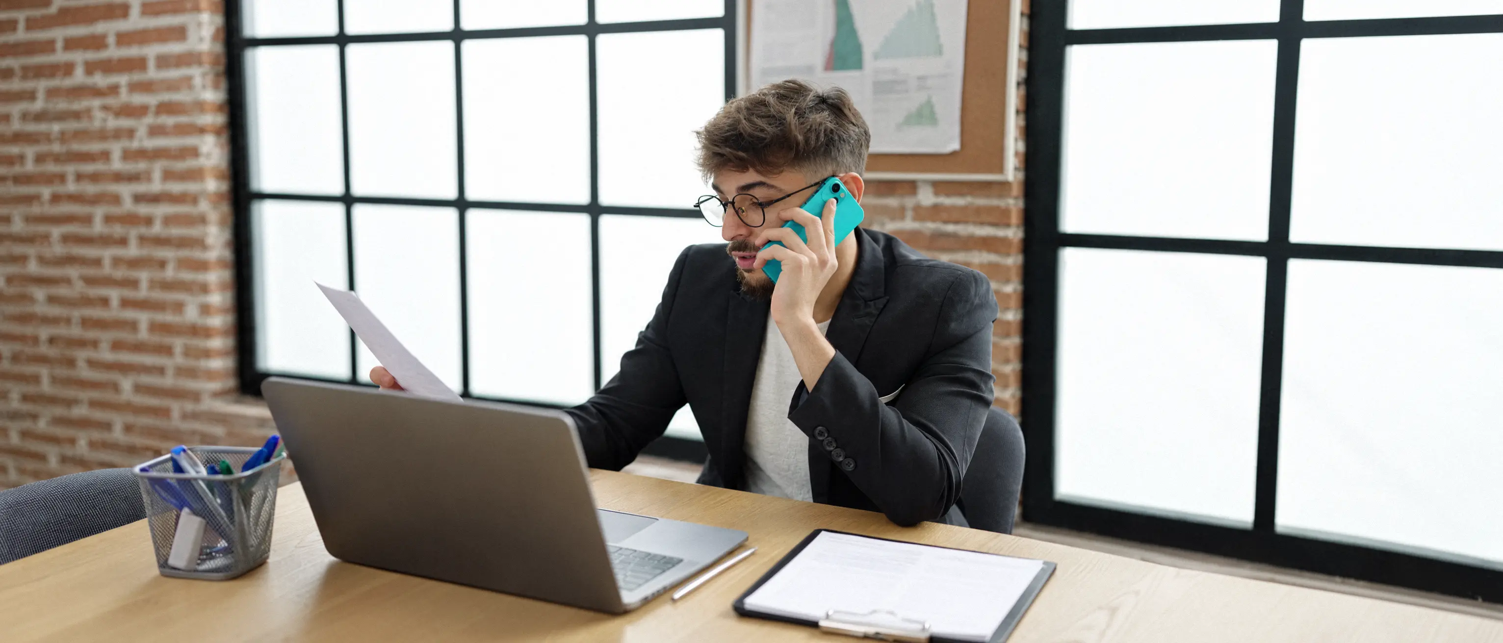 Un homme au téléphone, un document à la main, devant son ordinateur
