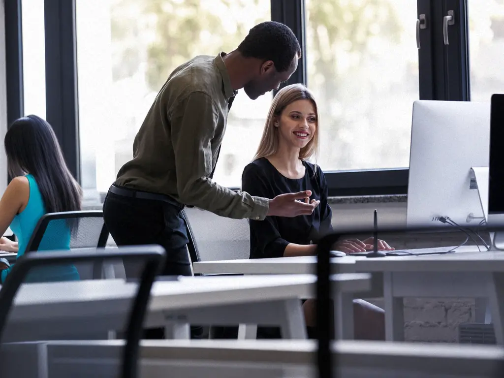 Deux collègues échangent devant un écran, dans un bureau lumineux