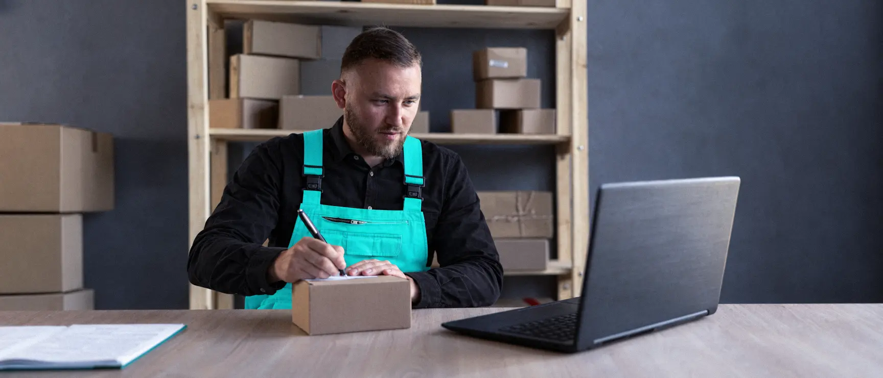 Un préparateur note une commande, ordinateur ouvert, dans une réserve